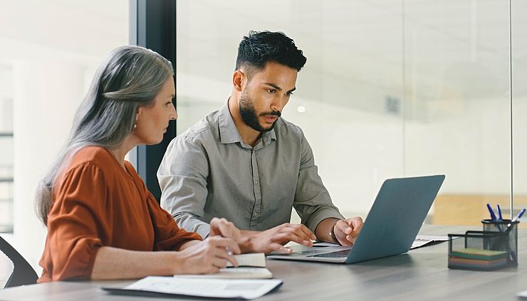 Ältere Frau und Junger Mann diskutieren am Laptop
