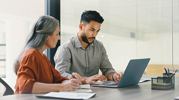 Ältere Frau und Junger Mann diskutieren am Laptop