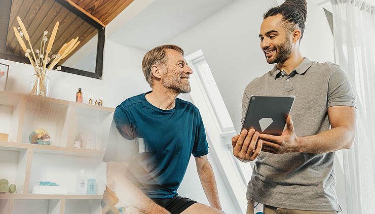 Physiotherapeut zeigt seinem Patienten etwas auf dem Tablet