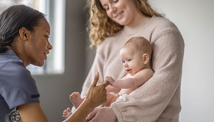 Baby auf dem Schoß seiner Mutter hält den Finger einer Hebamme