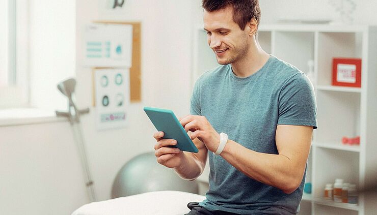 Physiotherapeut im Behandlungszimmer prüft etwas auf seinem Tablet