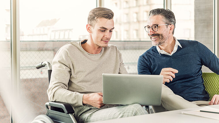 Zwei Männer sitzen fröhlich am Laptop.