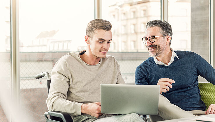 Zwei Männer sitzen fröhlich am Laptop.
