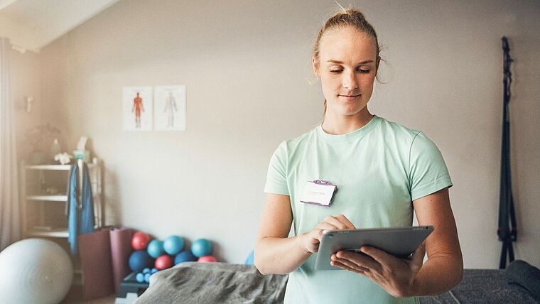 Eine Therapeutin steht in einer papierlosen Praxis mit einem Tablet in der Hand.