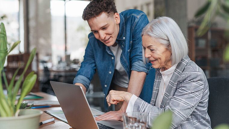 Ältere Frau und junger Mann bereiten eine Betriebsübernahme am Laptop vor