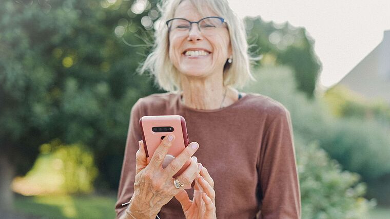Ältere Dame mit Smartphone freut sich über eine Nachricht