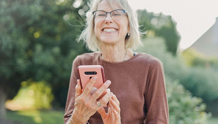 Ältere Dame mit Smartphone freut sich über eine Nachricht