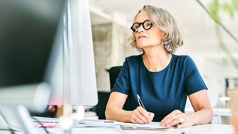 Frau mit Brille macht sich Notizen vor einem Computer