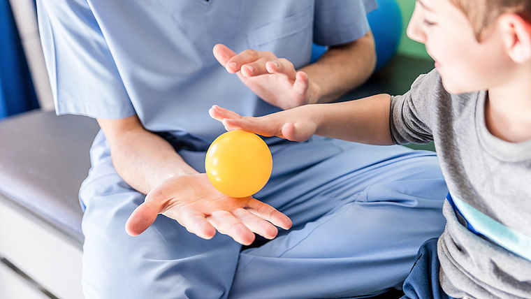 Ergotherapeutin macht Ballünbungen mit kleinem Jungen