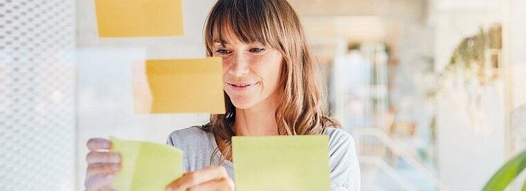 Junge Frau klebt Post-It Zettel an eine Wand