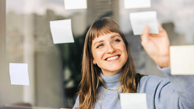 Eine Frau, möglicherweise Physiotherapeutin, klebt Post-Its an eine Glaswand