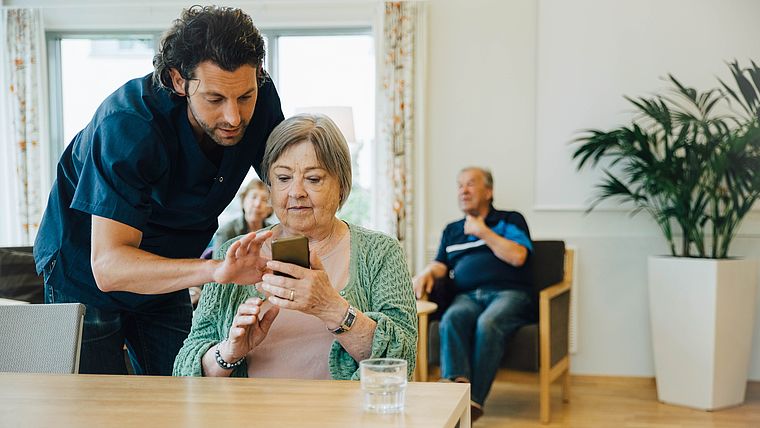 Pfleger erklärt Seniorin etwas am Smartphone