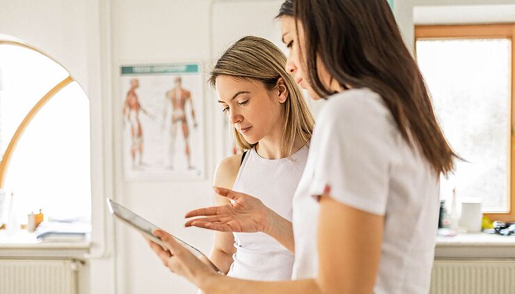 Physiotherapeutin zeigt ihrer Patientin etwas auf dem Tablet