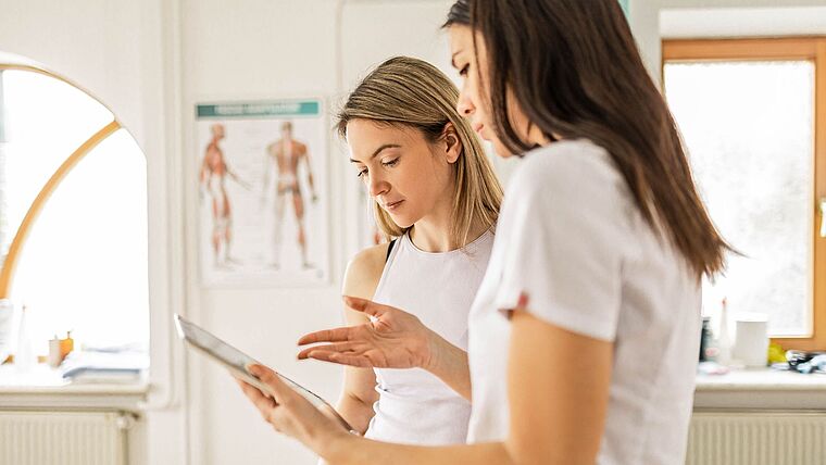 Physiotherapeutin zeigt ihrer Patientin etwas auf dem Tablet