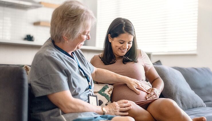 Hebamme berührt den Bauch einer schwangeren Frau