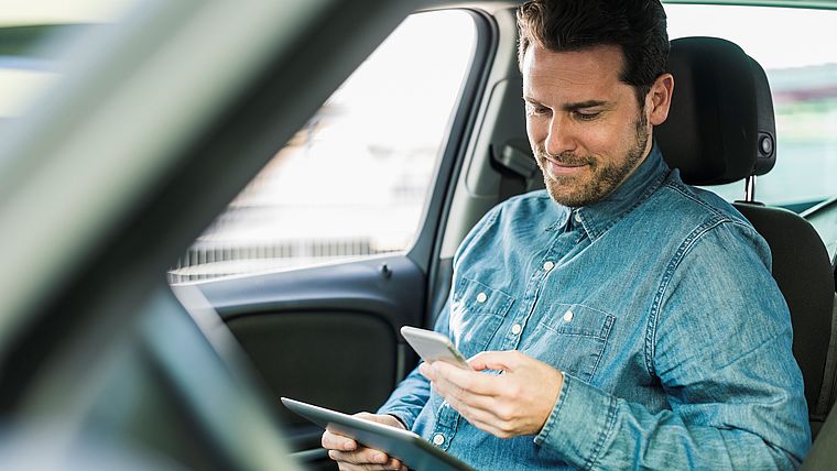 Junger Mann im Auto schaut auf sein Tablet