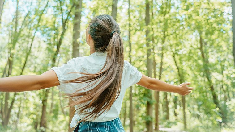 Frau steht mir ausgebreiteten Armen im Wald