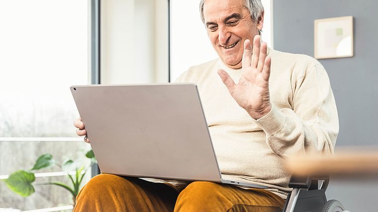 Senior im Rollstuhl mit Laptop auf dem Schoß