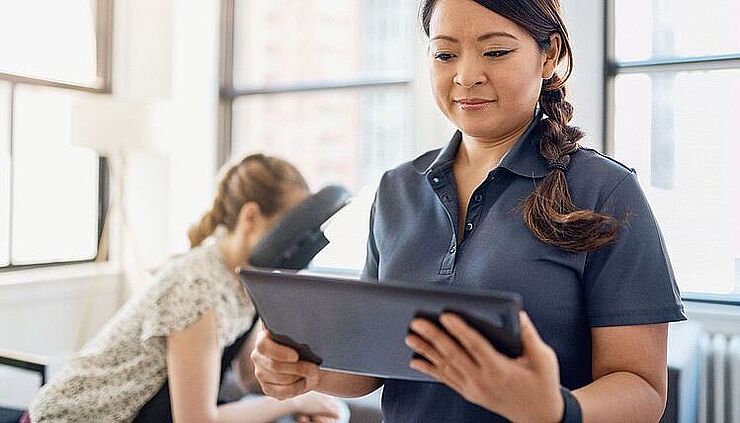 Physiotherapeutin schaut auf ihr Tablet, im Hintergrund Patientin wartend auf Behandlungsstuhl
