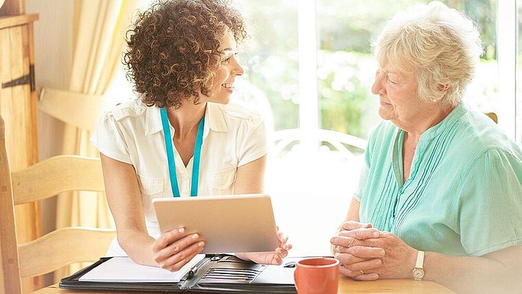 Weibliche Pflegekraft mit einem Tablet in der Hand bei einer älteren Patientin zu Hause